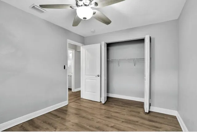 an empty room with wooden floor fan and windows