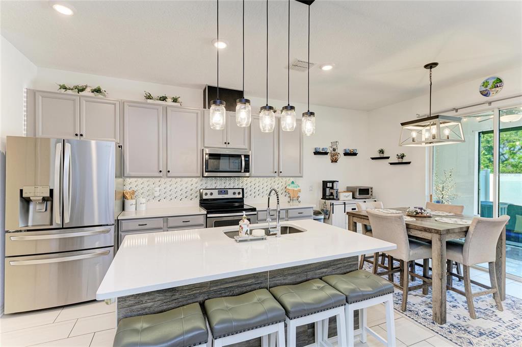 11637 Woodleaf Drive Lakewood Ranch, FL 34211 - Photo 13 of 54 a kitchen with stainless steel appliances kitchen island granite countertop a dining table chairs and a refrigerator