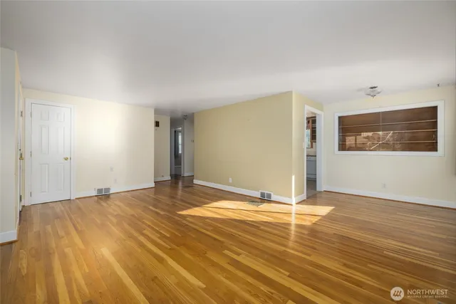 a view of an empty room with window and wooden floor