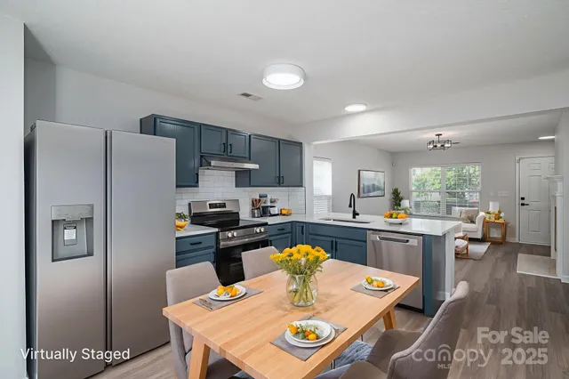 a kitchen with stainless steel appliances granite countertop a refrigerator a stove a sink a dining table and chairs with wooden floor