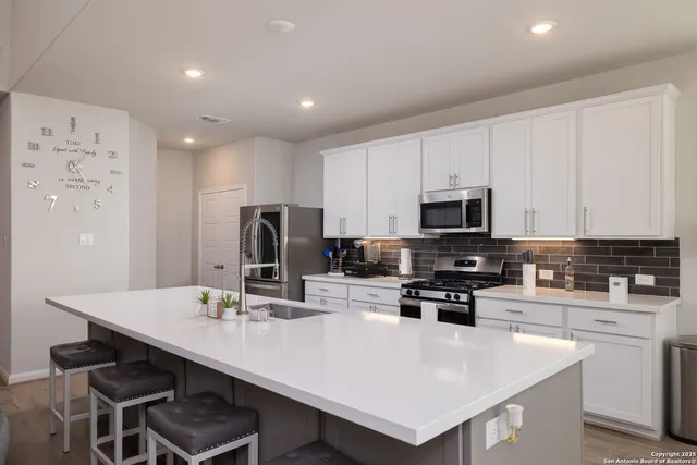 a kitchen with stainless steel appliances a stove a sink a microwave a refrigerator and white cabinets