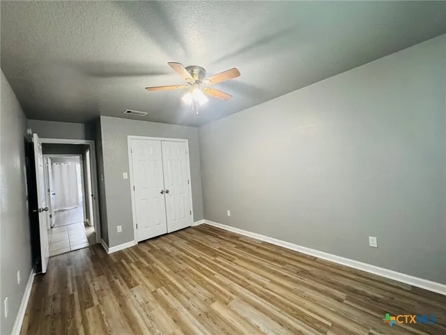 an empty room with wooden floor fan and windows