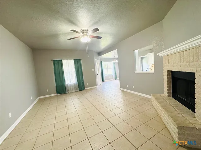 a view of an empty room with chandelier fan and fire place