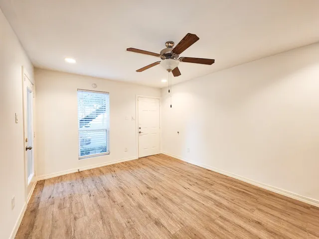 an empty room with wooden floor fan and windows