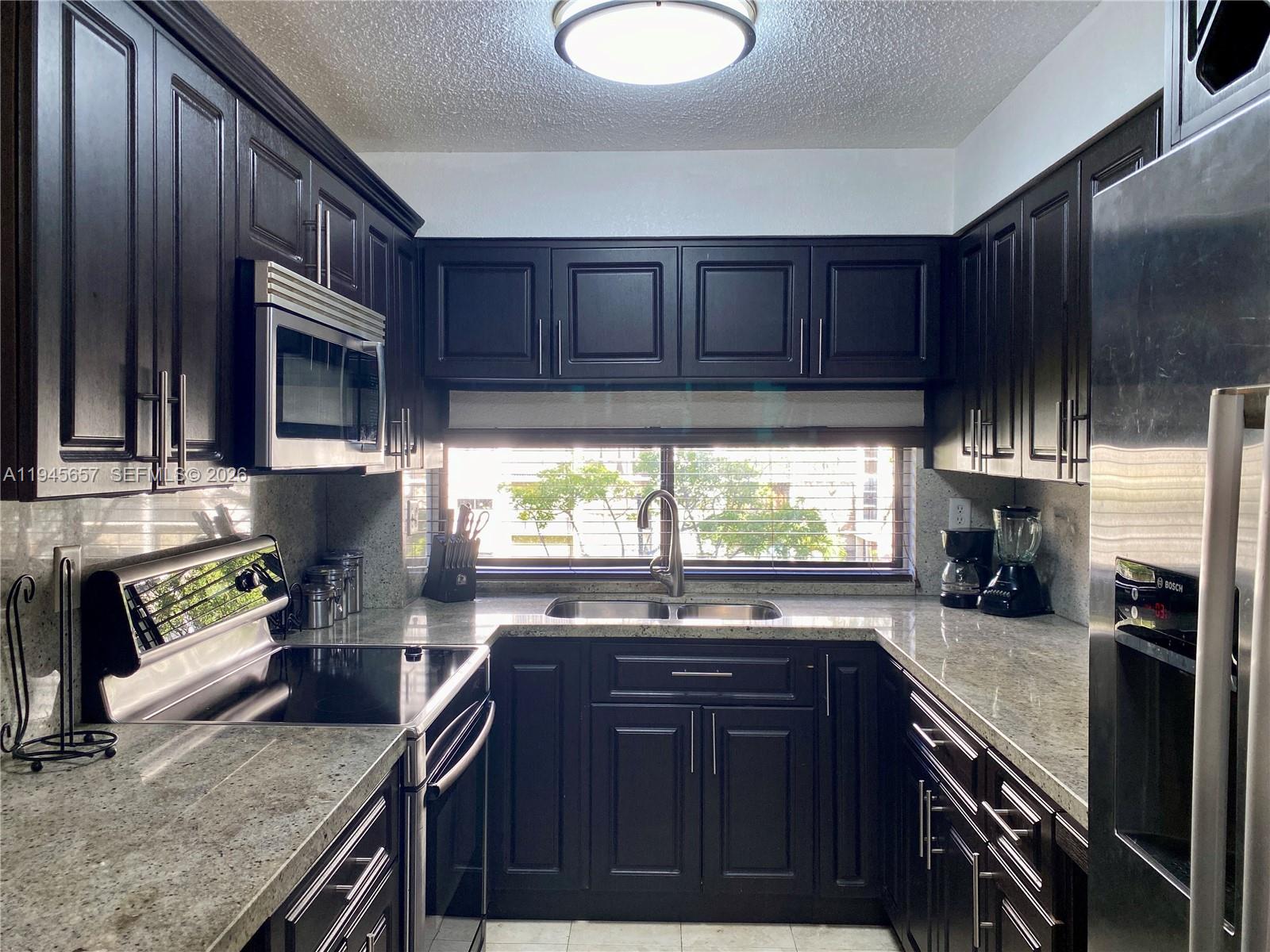 17011 North Bay Road, Unit 304 Sunny Isles Beach, FL 33160 - Photo 11 of 54 a kitchen with granite countertop wooden cabinets a stove top oven a sink and dishwasher