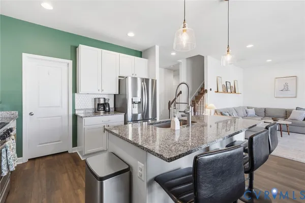 a kitchen with stainless steel appliances granite countertop a kitchen island a stove a refrigerator a dining table and chairs with wooden floor