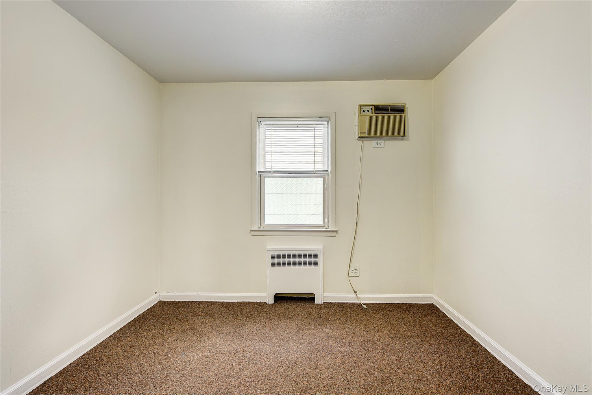 163-02 45th Avenue Queens, NY 11358 - Photo 15 of 35 Spare room featuring radiator, dark colored carpet, and a wall unit AC
