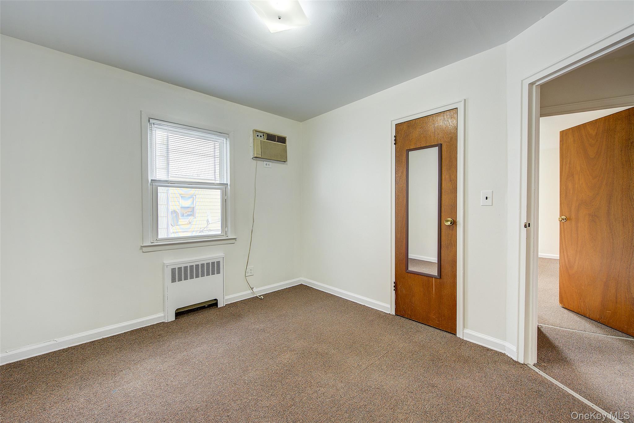 163-02 45th Avenue Queens, NY 11358 - Photo 16 of 35 Spare room with radiator heating unit, carpet, and an AC wall unit