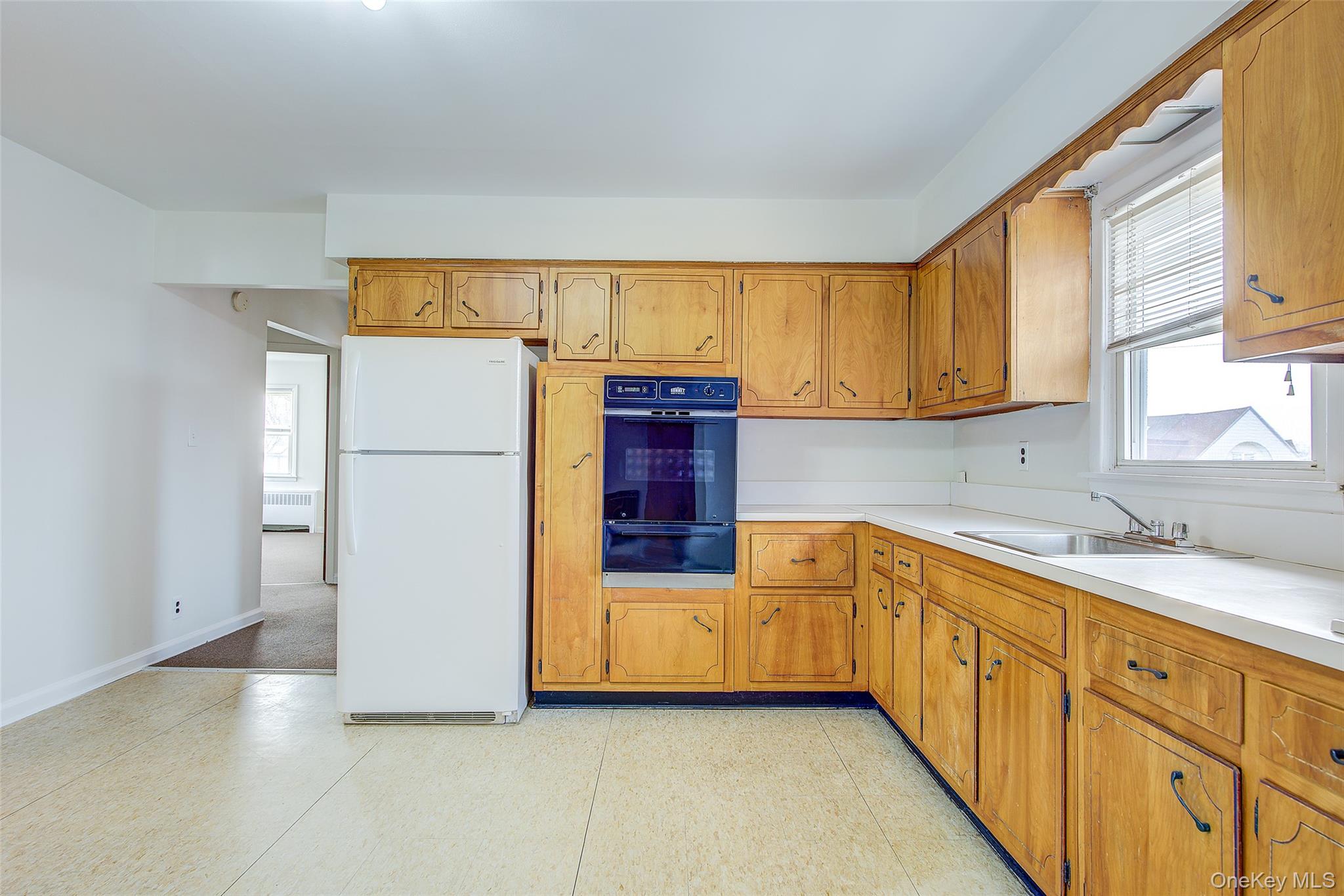 163-02 45th Avenue Queens, NY 11358 - Photo 9 of 35 Kitchen with freestanding refrigerator, light countertops, oven, brown cabinetry, and radiator