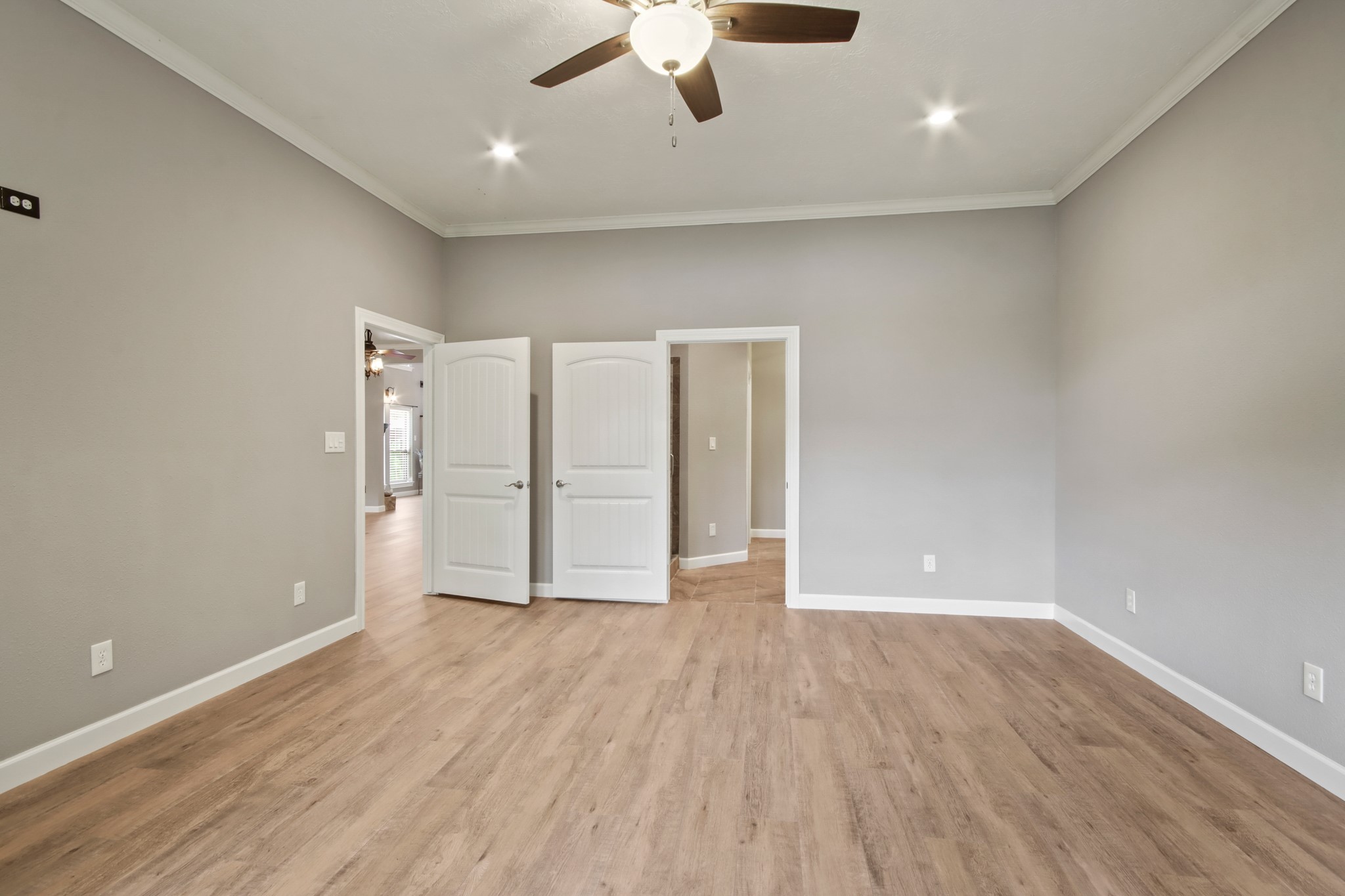 35 Susan Drive Cleveland, TX 77327 - Photo 10 of 33 This spacious room features light wood flooring, neutral gray walls, and a ceiling fan with recessed lighting. Double doors lead to an adjacent area, enhancing the open, airy feel.