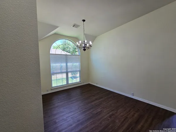 an empty room with wooden floor chandelier and windows