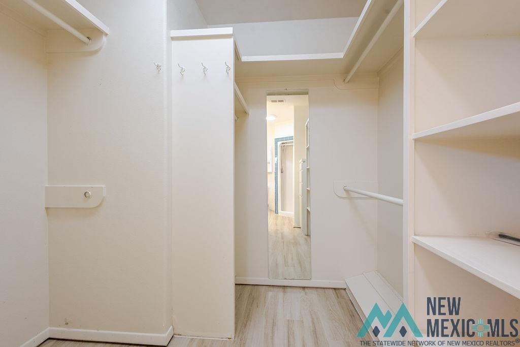 1131 Curry Road North Clovis, NM 88101 - Photo 29 of 69 Walk-in closet featuring wood-finish flooring, built-in shelving, multiple hanging rods, and an integrated full-length mirror