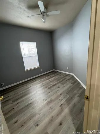 an empty room with wooden floor fan and windows