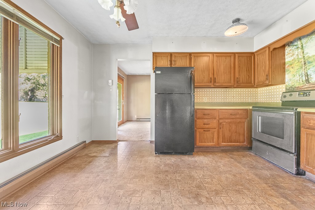 Kitchen with a baseboard heating unit, ceiling fan, backsplash, black refrigerator, and range with electric cooktop
