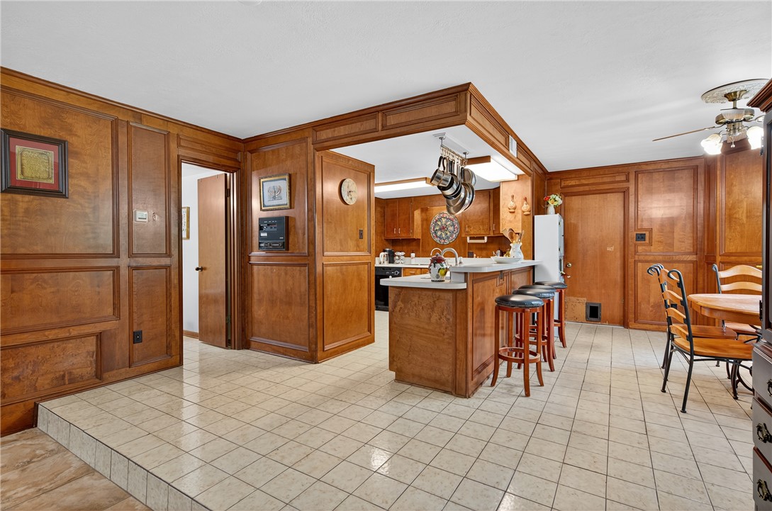 3501 Broad Oak Circle Bryan, TX 77802 - Photo 5 of 28 Kitchen with a breakfast bar, light countertops, brown cabinets, wooden walls, and light tile patterned flooring