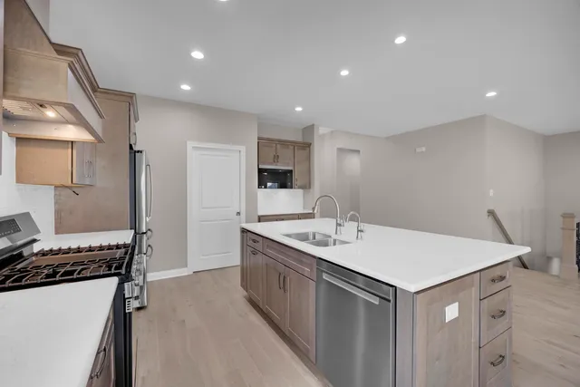 a kitchen with stainless steel appliances granite countertop a stove top oven a sink dishwasher a refrigerator and a dining table with wooden floor