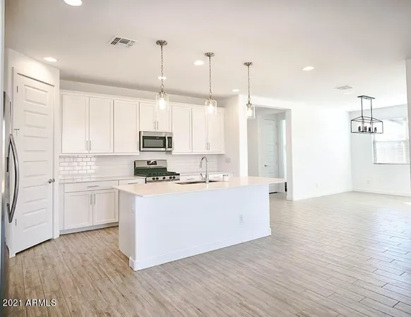 a kitchen with stainless steel appliances granite countertop a sink a stove a refrigerator and white cabinets with wooden floor