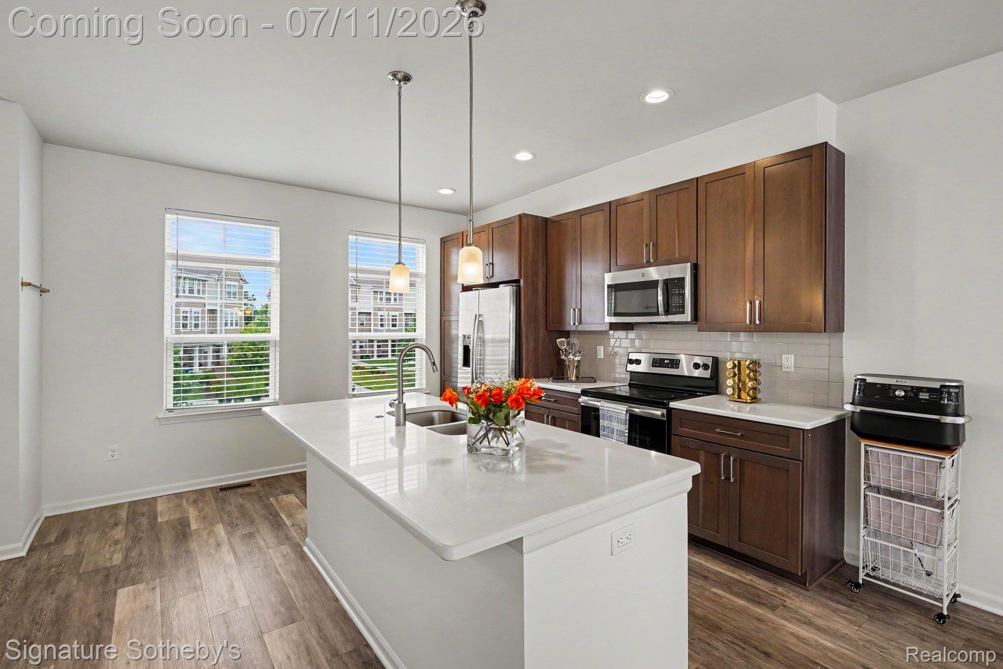 2500 Normandy Road, Unit 40 Royal Oak, MI 48073 - Photo 10 of 26 Modern kitchen featuring a central island with a sink, stainless steel appliances, rich wood cabinetry, a tile backsplash, and wood-finish flooring