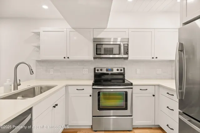 a kitchen with stainless steel appliances granite countertop white cabinets a stove a sink and a white refrigerator