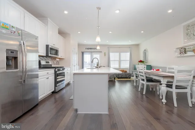 a kitchen with stainless steel appliances granite countertop a stove top oven a refrigerator a sink and a dining table with wooden floor