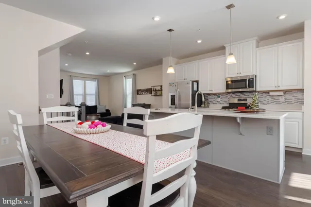 a kitchen with stainless steel appliances granite countertop a stove a sink a refrigerator and a dining table with wooden floor