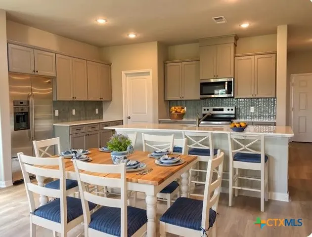 a kitchen with stainless steel appliances kitchen island granite countertop a table chairs and a refrigerator