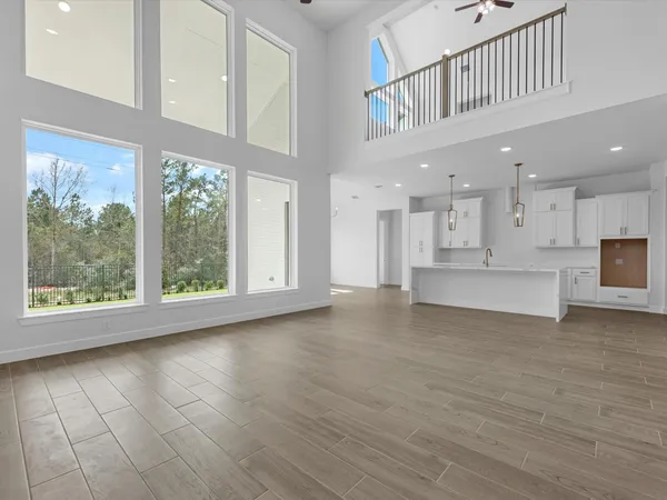 a view of an empty room with kitchen view and wooden floor