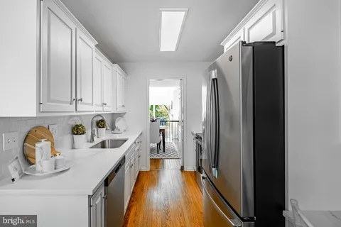 a kitchen with stainless steel appliances granite countertop a refrigerator a sink and white cabinets with wooden floor