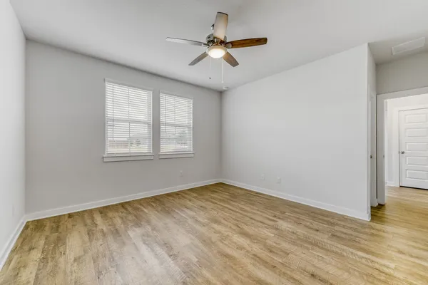 an empty room with wooden floor chandelier fan and windows