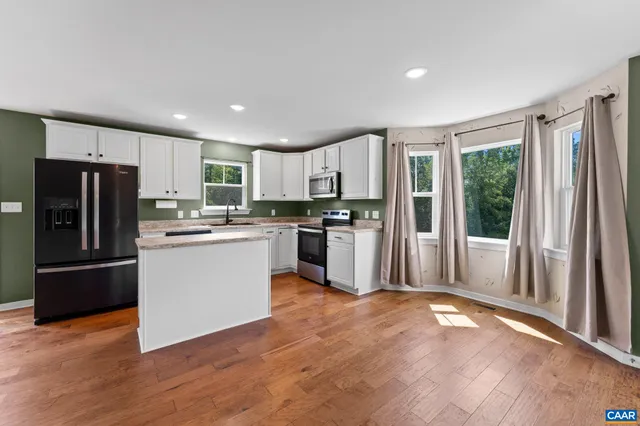 a kitchen with stainless steel appliances granite countertop a refrigerator a sink dishwasher a stove with wooden floors and a large window