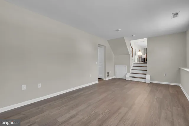 a view of an empty room with wooden floor and stairs