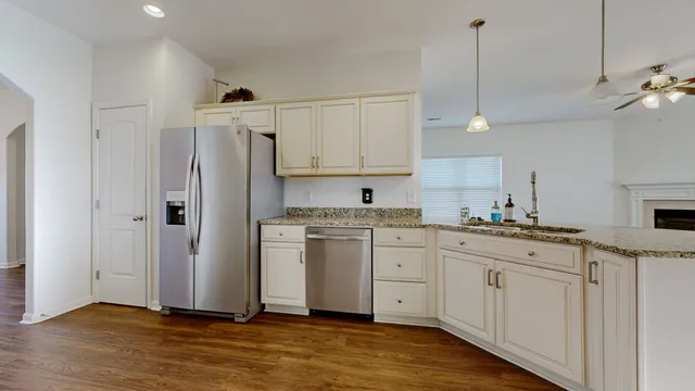 a kitchen with stainless steel appliances granite countertop a refrigerator a sink dishwasher and white cabinets with wooden floor