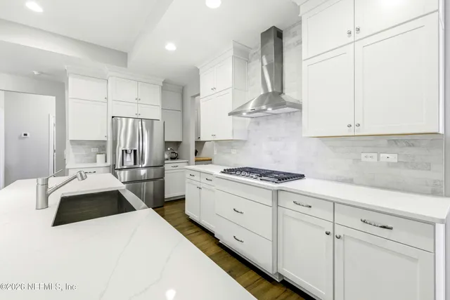 a kitchen with stainless steel appliances granite countertop a sink a stove a refrigerator and white cabinets
