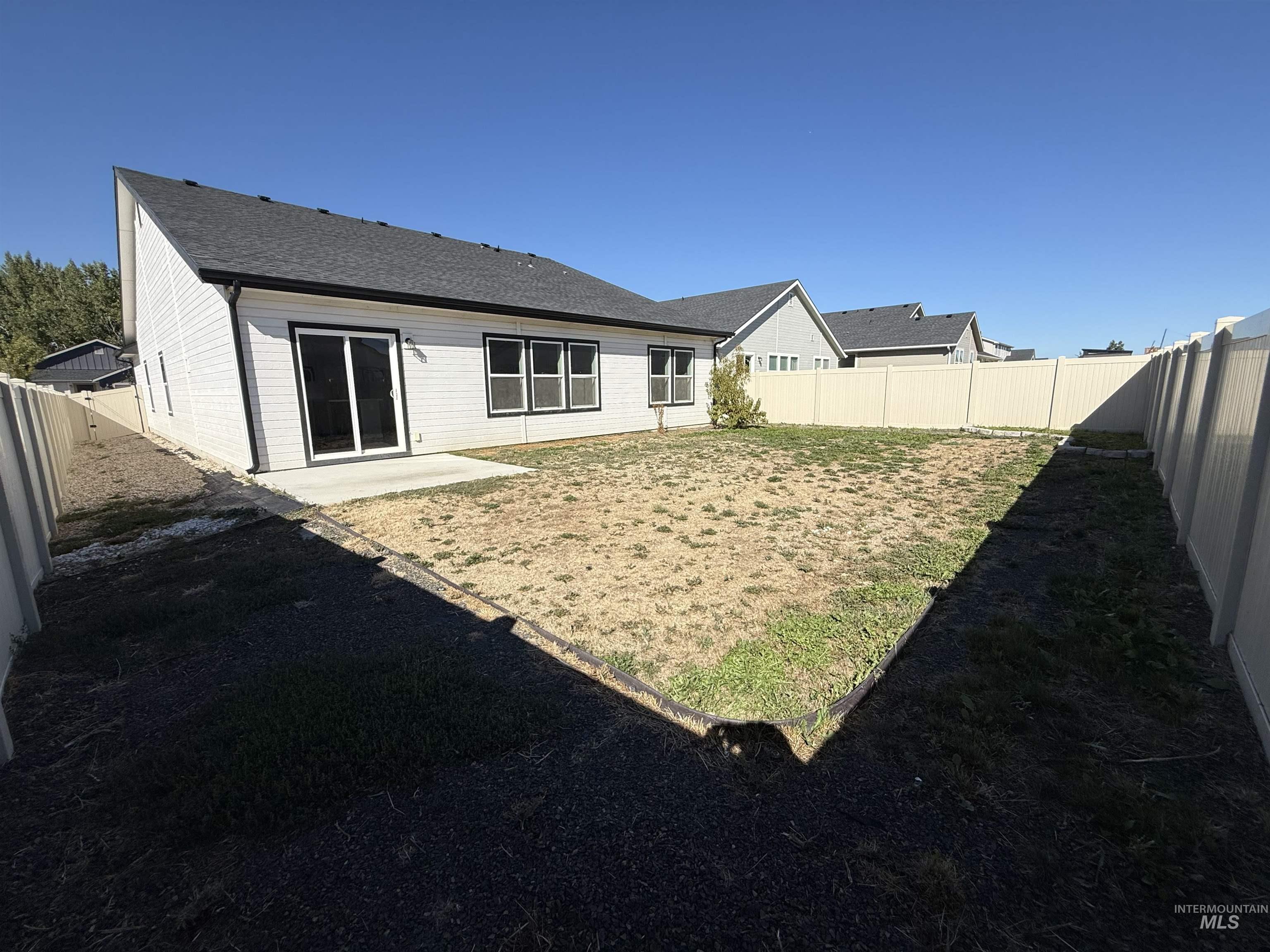 12451 Varga Street Caldwell, ID 83607 - Photo 27 of 30 Rear exterior featuring white siding, black-framed windows, a concrete patio, and a privacy fence