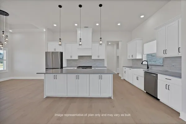 a large white kitchen with stainless steel appliances granite countertop a stove a sink a refrigerator and white cabinets
