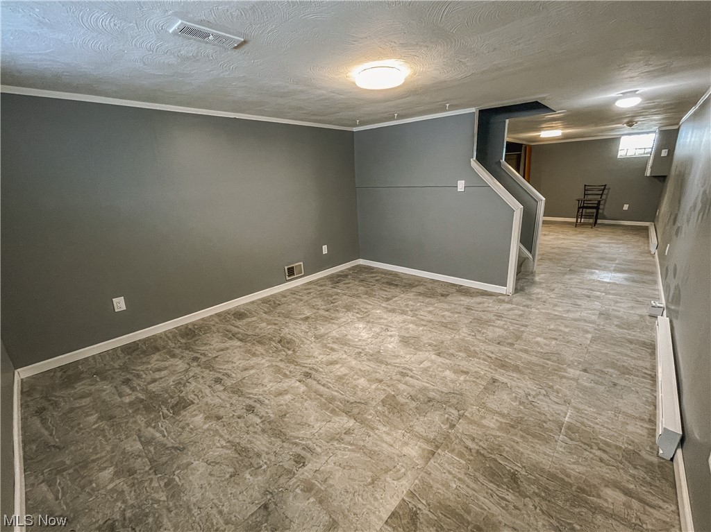 24709 Emery Road Warrensville Heights, OH 44128 - Photo 26 of 34 Basement with ornamental molding, light tile floors, a baseboard heating unit, and a textured ceiling