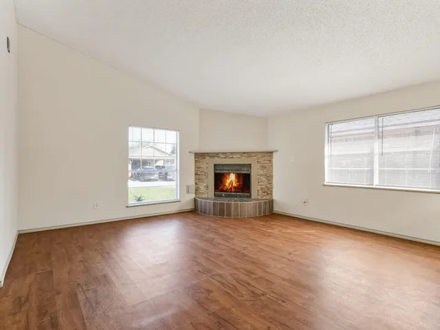 an empty room with wooden floor fireplace and windows