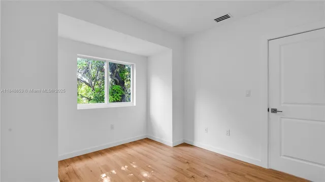 a view of an empty room with wooden floor and a window