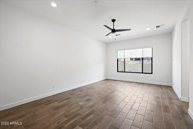 an empty room with wooden floor ceiling fan and windows