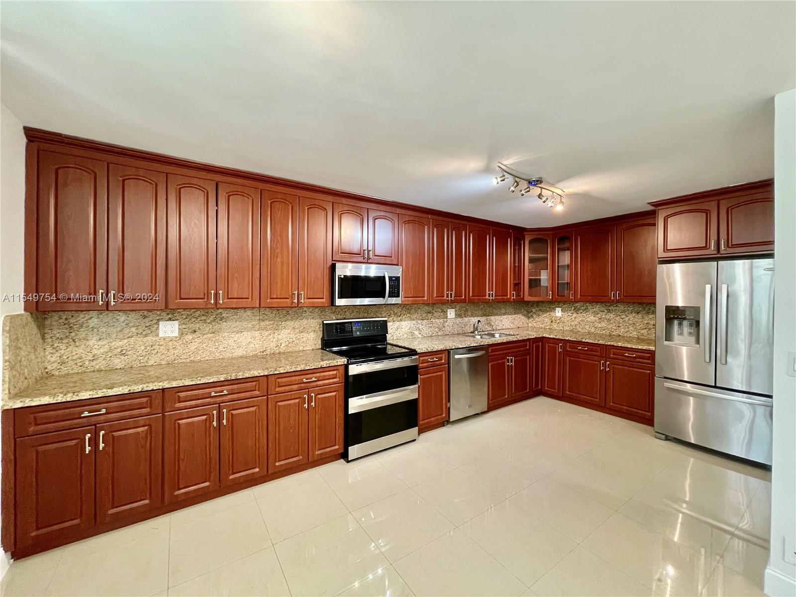 a large kitchen with granite countertop stainless steel appliances and wooden cabinets