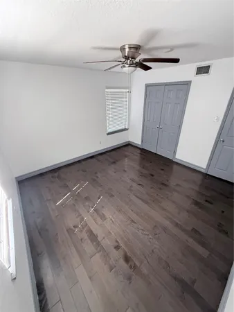 an empty room with wooden floor fan and windows