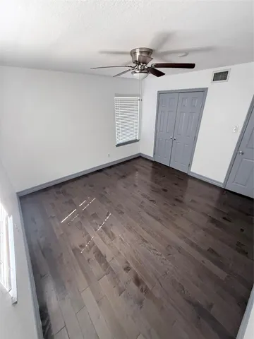 an empty room with wooden floor fan and windows