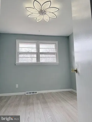 an empty room with wooden floor chandelier fan and windows