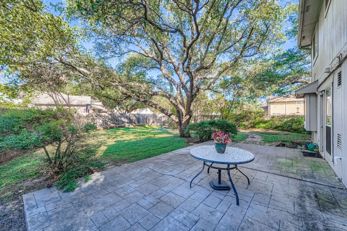 a view of a backyard with table and chairs potted plants and large tree