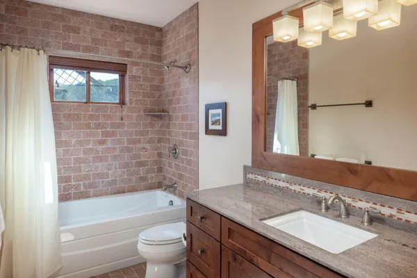 a bathroom with a granite countertop sink a toilet a mirror a bathtub and shower