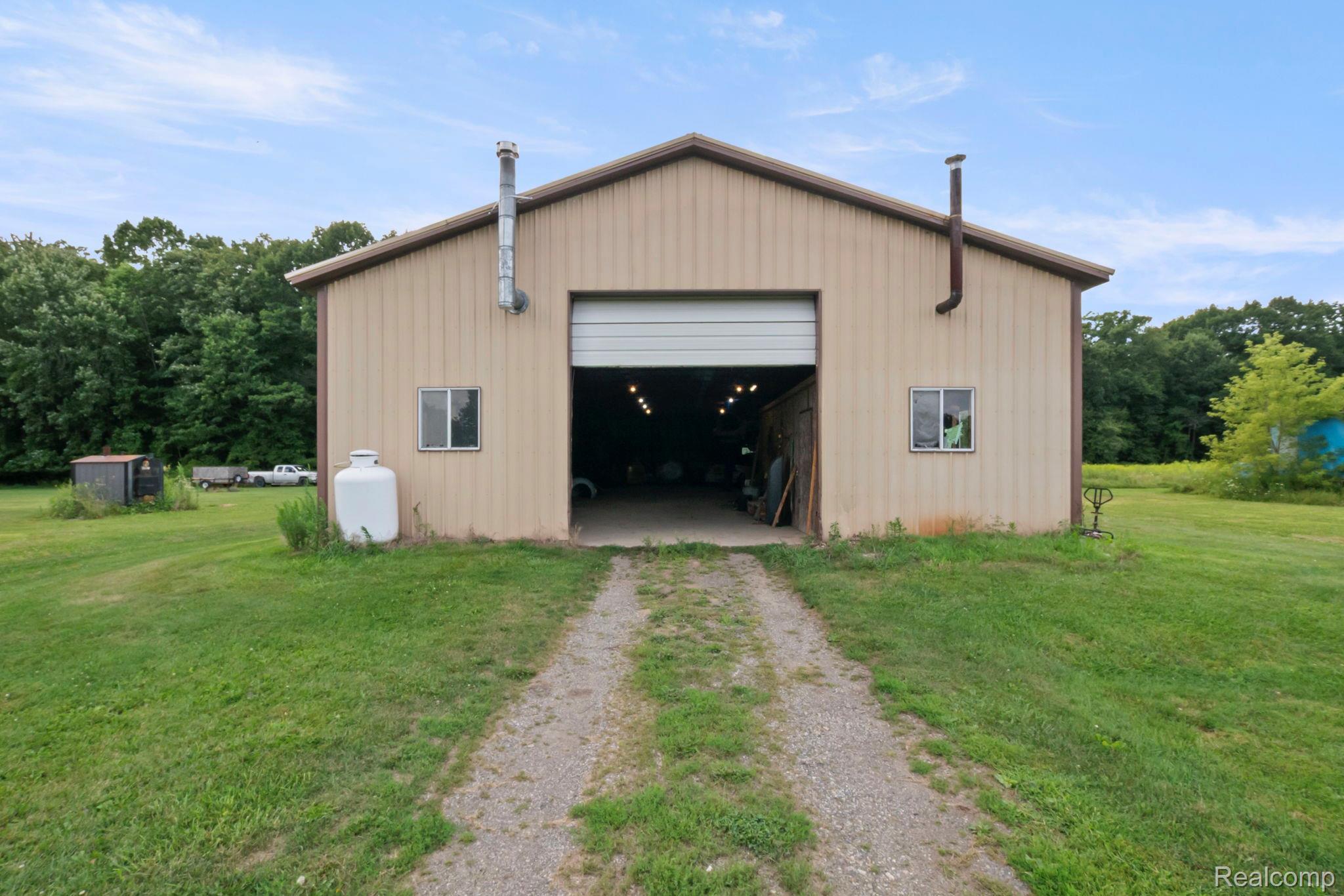 76565 McFadden Road Armada, MI 48005 - Photo 58 of 95 Metal-sided outbuilding featuring a large roll-up door, two windows, and a gravel driveway