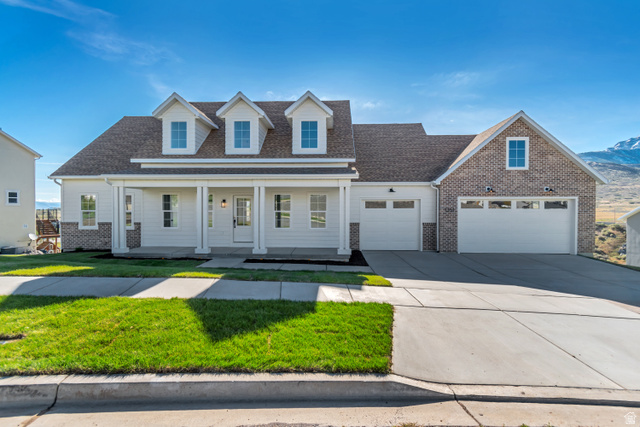 Exterior featuring white siding, brick accents, a covered front porch with columns, a two-car garage, and an additional one-car garage