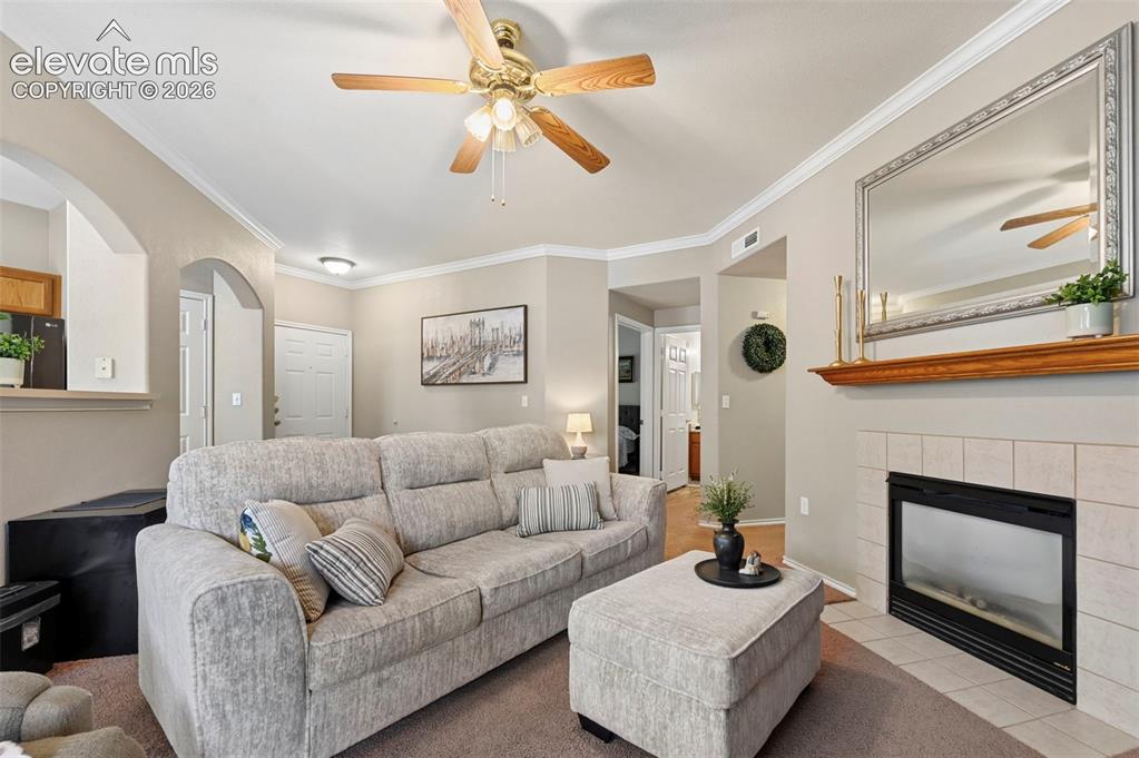 3715 Riviera Grove, Unit 101 Colorado Springs, CO 80922 - Photo 16 of 36 Living room featuring a ceiling fan, crown molding, arched doorways, a fireplace with a tile surround, and a wood mantel