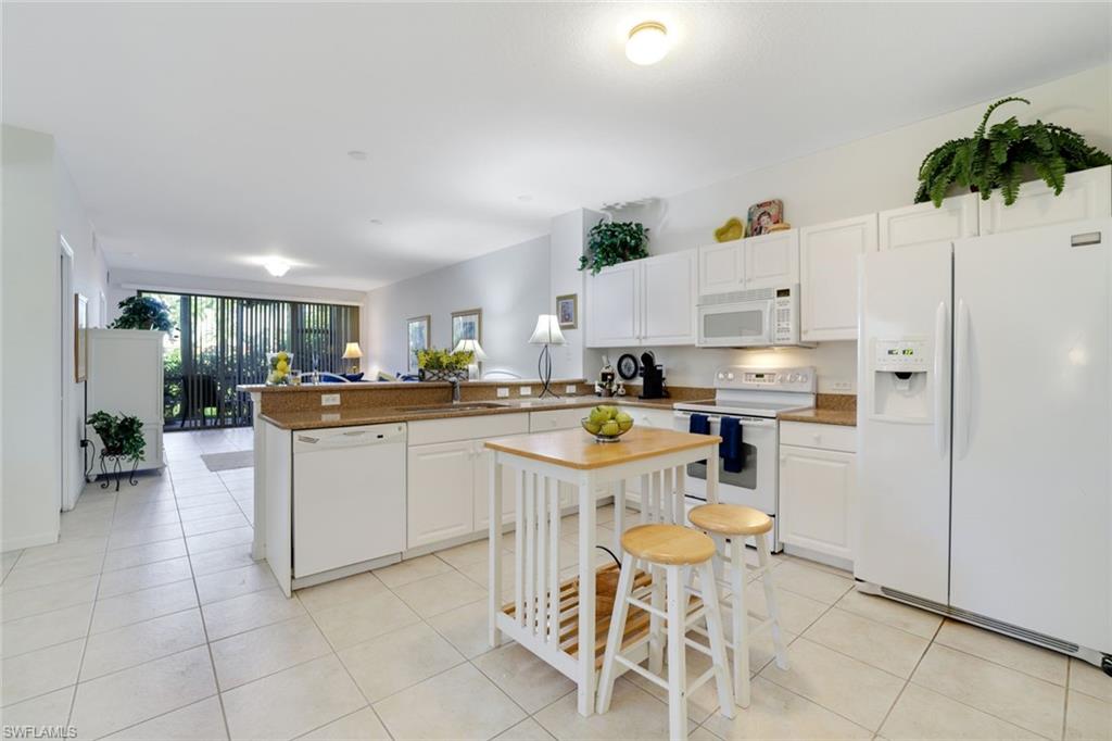 10049 Heather Lane, Unit 101 Naples, FL 34119 - Photo 14 of 28 Kitchen featuring white appliances, white cabinetry, a peninsula, light tile patterned floors, and expansive windows