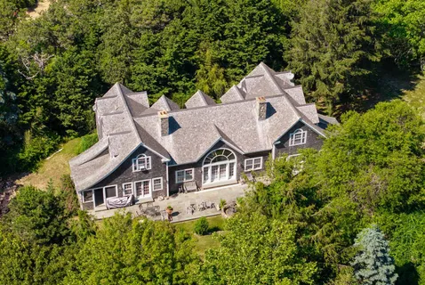 an aerial view of a house with yard and trees in the background
